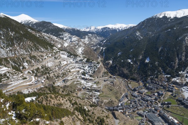 Verschneite Berge und ein Tal mit Straßen und verstreuten Gebäuden unter einem klaren blauen Himmel