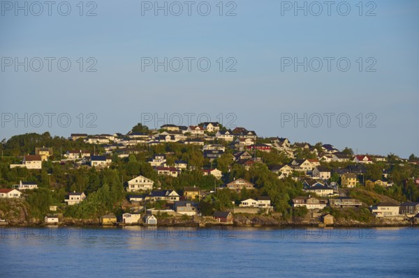 Small wooded island with houses in the sea with clear skies and calm water, Strusshamn, Bergen,