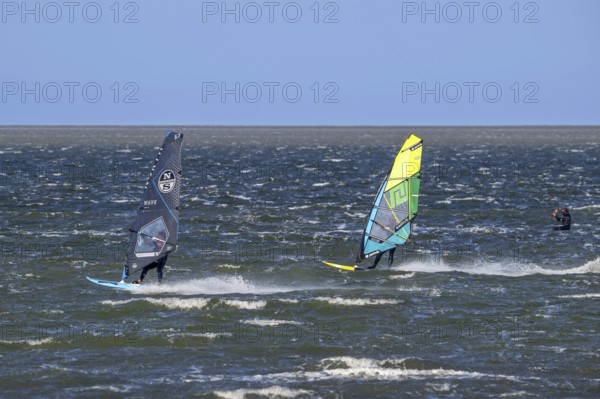 Kiteboarder, kitesurfer and two recreational windsurfers in wetsuits practising classic windsurfing