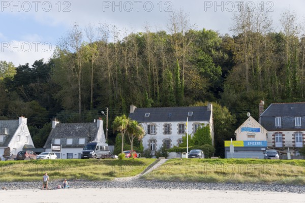Beach view with houses and shops on the coast, surrounded by green trees, Plage Saint Efflamm,
