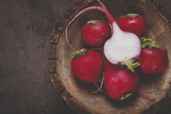 Fresh red radishes are displayed on a rustic wooden cutting board, highlighting their smooth skins