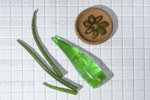 Aloe vera leaves and a container of aloe gel arranged on white bathroom tiles, symbolizing natural