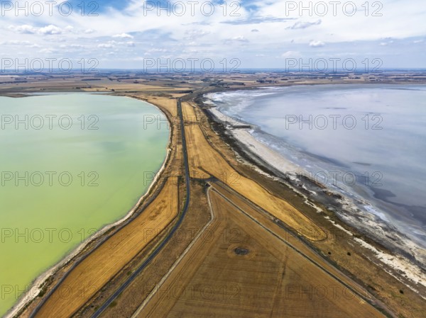 Aerial photo contrasting vibrant green and gray lakes divided by roads and golden fields in
