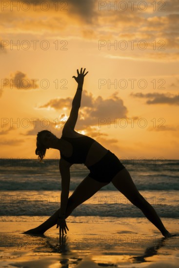 A serene silhouette of a woman practicing yoga on a beach during sunset in Tulum, Mexico. The warm