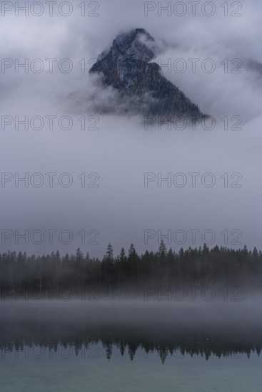 A stunning view of a mountain peak in Hintersee, partially shrouded in fog, surrounded by serene