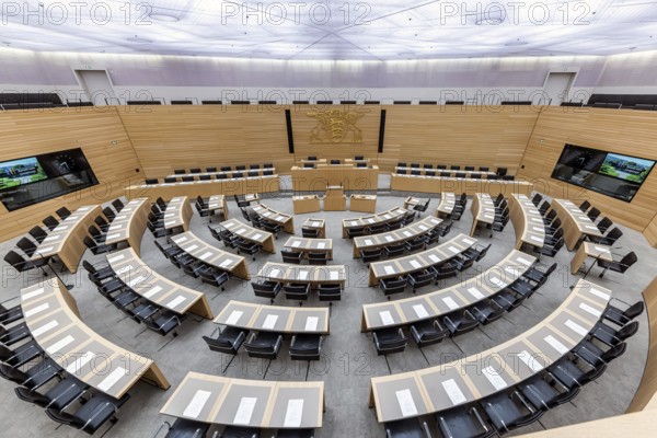 Plenary hall deserted with the seats of deputies and the government bank. Behind it is the coat of