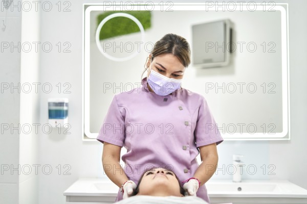 A skilled practitioner wearing a mask provides a facial treatment to a client in a modern beauty