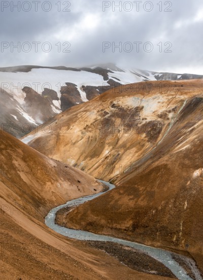 Steaming stream between colourful rhyolite mountains and snowfields, Hveradalir geothermal area,