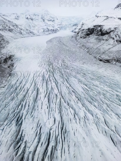 Aerial view of Icelandic winter landscape featuring a vast, icy glacier with intricate patterns.