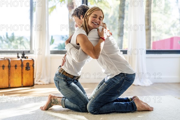 Side view of a man and a woman, both smiling, embrace warmly in a bright, airy room, expressing