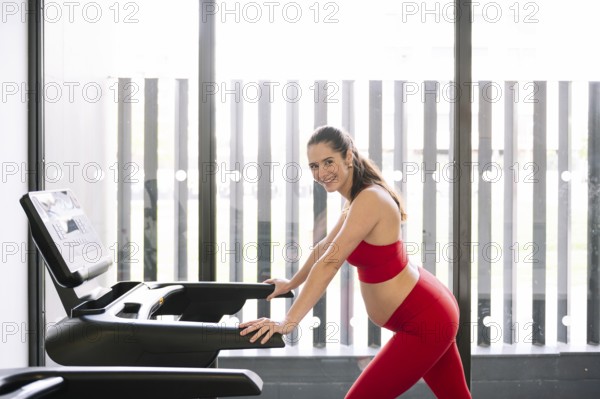 Pregnant woman in a red sports outfit exercising on a treadmill, promoting pregnancy wellness and