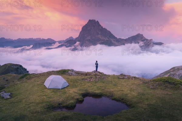 A camper stands near a tent overlooking a majestic mountain peak above a sea of clouds during a