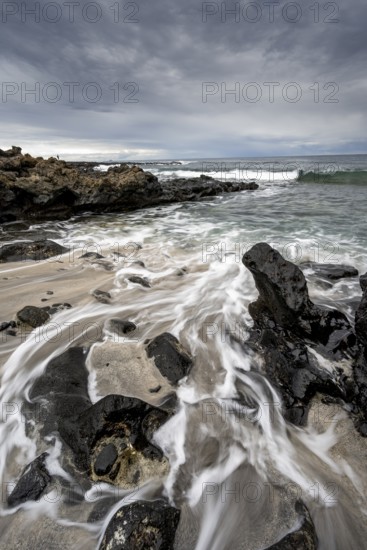 Waves blaze on the beach, rocky coast with volcanic stones, long exposure, Playa de la Pequeña,