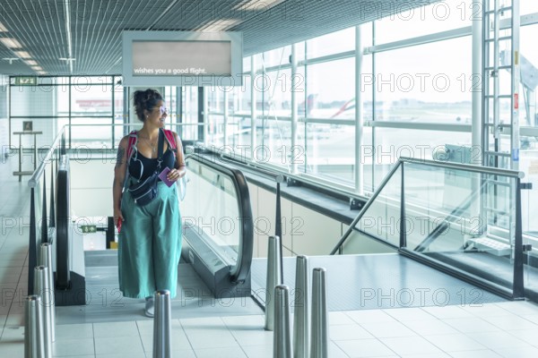A traveler stands on an escalator in a bright airport, holding a passport, A sign above wishes you