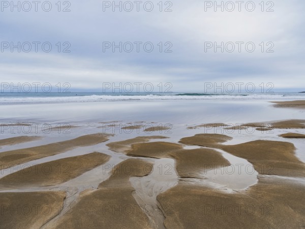 Serene coastal landscape featuring expansive sandy shores and reflective tidal pools under a cloudy