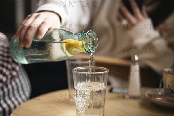 Cropped unrecognizable girl pours water from a bottle with a slice of lemon into a glass in a cafe,