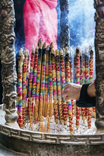 Cropped unrecognizable person holding a vibrant, large incense sticks burning, with smoke rising in