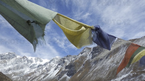 Colourful prayer flags flying in close-up against a background of a snowy mountain range, hiking in