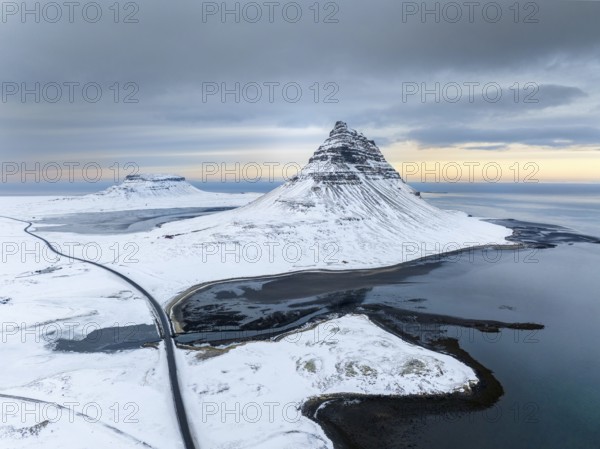 A breathtaking aerial view of Kirkjufell mountain in Iceland, covered in snow, surrounded by icy