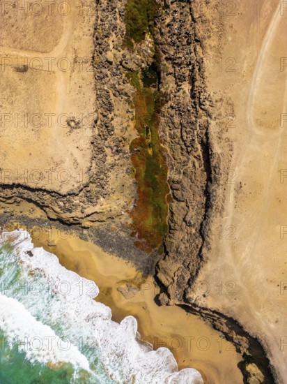 From above, an aerial shot captures a striking natural pool nestled within the rugged coastal