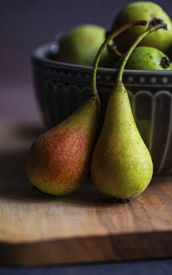 Close up of two wild pears resting on a wooden board with a decorative ceramic bowl filled with