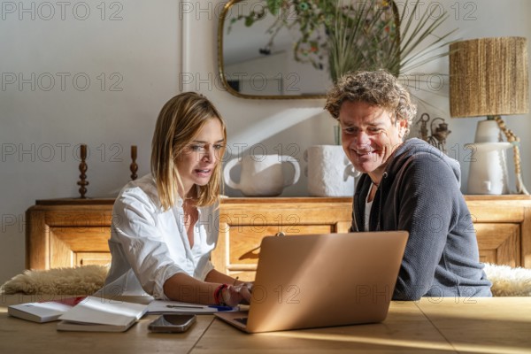 A couple works together at home, focused on a laptop The setting is cozy with a warm atmosphere,