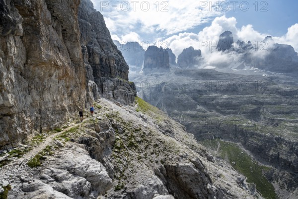 Two mountaineers on a hiking trail in front of a picturesque mountain landscape with rocky peaks,