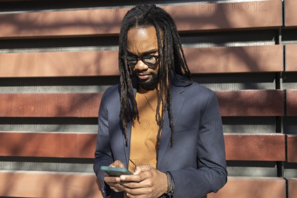 A cuban business professional with glasses and dreadlocks stands outdoors in sunlight, using a