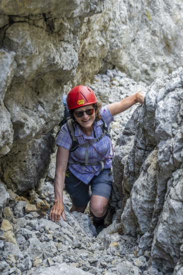 Female mountaineer with helmet climbing a rock face, ascent to the Ackerlspitze, Wilder Kaiser,