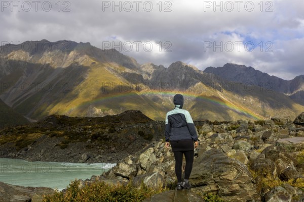 A woman stands on rocky terrain, admiring a vibrant autumn landscape on Mount Cook, New Zealand,