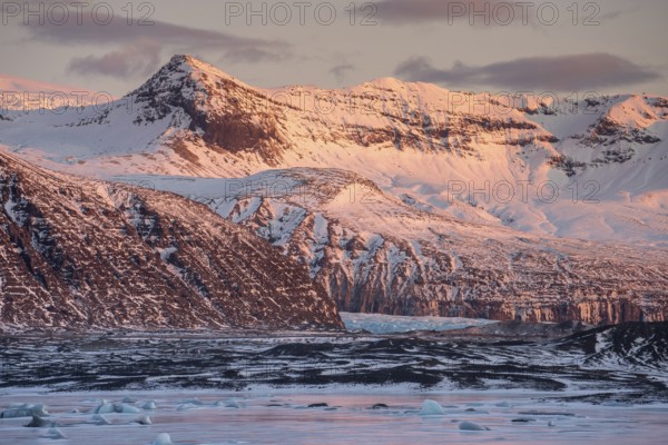 A breathtaking winter sunrise casts a warm glow over the snow-capped mountains and icy landscape in