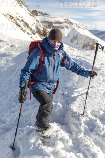 Adventurer in blue jacket and red backpack enjoys ski touring on a sunny day. Using poles for