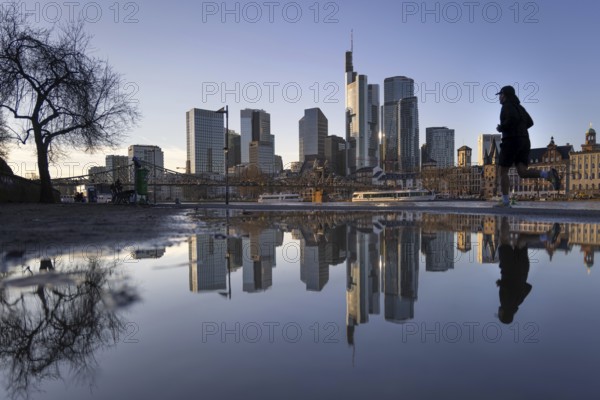Frankfurt's banking skyline and a jogger running by are reflected in a puddle on the banks of the
