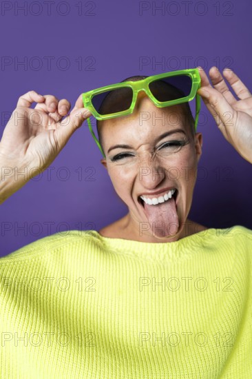 A vibrant middle aged woman with a shaved head wearing bright green sunglasses and a yellow sweater