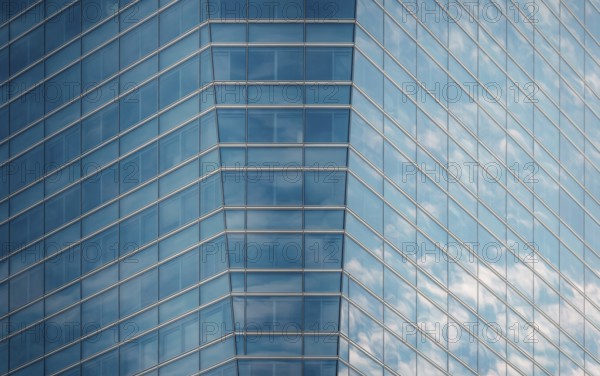 Close-up of a modern glass building facade reflecting a clear blue sky and fluffy clouds,