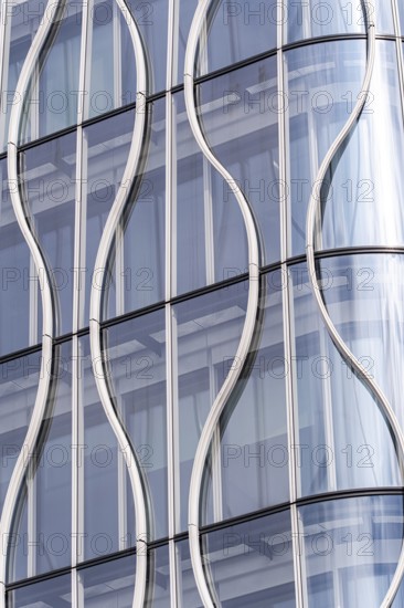 Close-up of a modern building facade, showcasing wavy glass panels and sleek metal frames. The