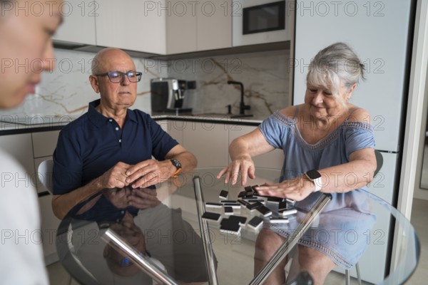 A multigenerational family gathers around a kitchen table, enjoying a lively game of dominoes.