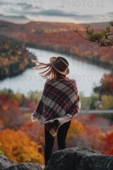 A woman in a hat and plaid shawl stands overlooking a picturesque Quebec landscape in autumn. The