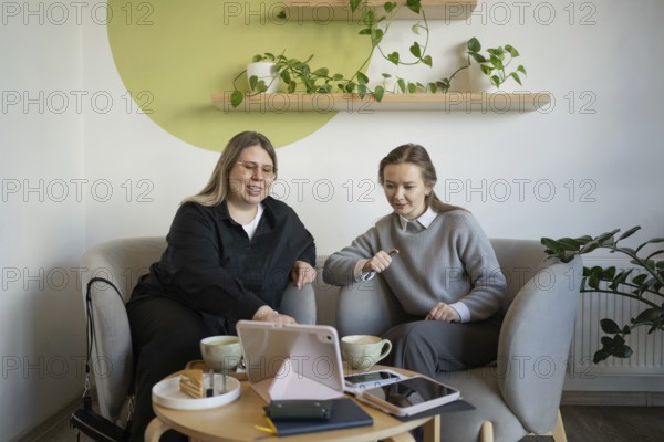 Two women sit in a cozy cafe, enjoying coffee and conversation. Laptops and notebooks are on the