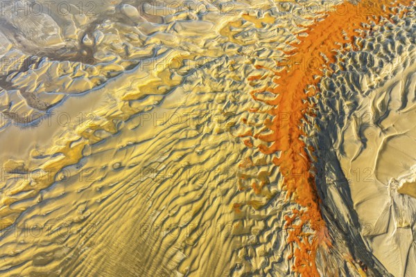 Aerial image showcasing striking orange and yellow sand patterns resembling waves on a beach,