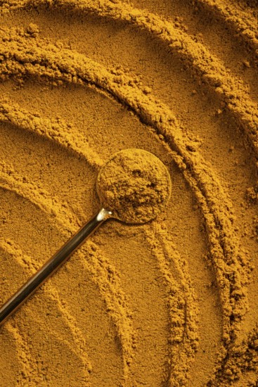 A vibrant close-up of golden curry powder, showcasing its textured surface with swirling patterns