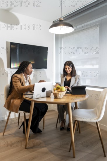 Two businesswomen are working together on their laptops and tablets in a hotel room, enjoying a