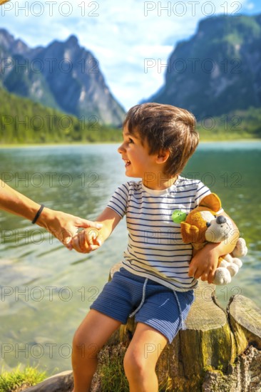 Smiling child holding a plush toy and his parent's hand while enjoying a summer day at lake