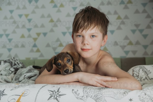 A young boy, with thoughtful blue eyes, gently holds his small Dachshund puppy as they relax