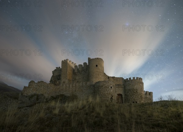 Night falls over the Manqueospese Castle in Avila, Spain, with star trails shimmering above its
