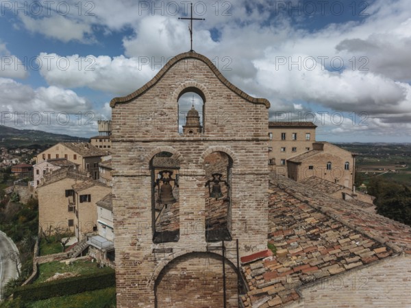 A historic bell tower stands amid rustic rooftops in Treia, Italy. The brick architecture contrasts