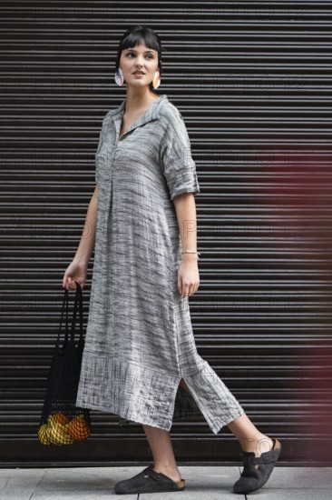 A fashionable woman walks confidently in the city while carrying a black bag with oranges and