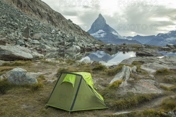 A vibrant green tent is set by a tranquil alpine lake, with the majestic Matterhorn towering in the