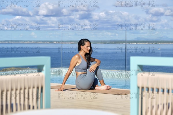 A woman practices yoga on a deck overlooking a vast ocean, enjoying a peaceful environment. The