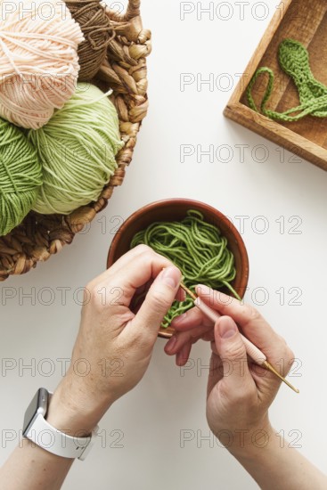 Top view of cropped unrecognizable hands crocheting with a pink hook and green yarn in a creative